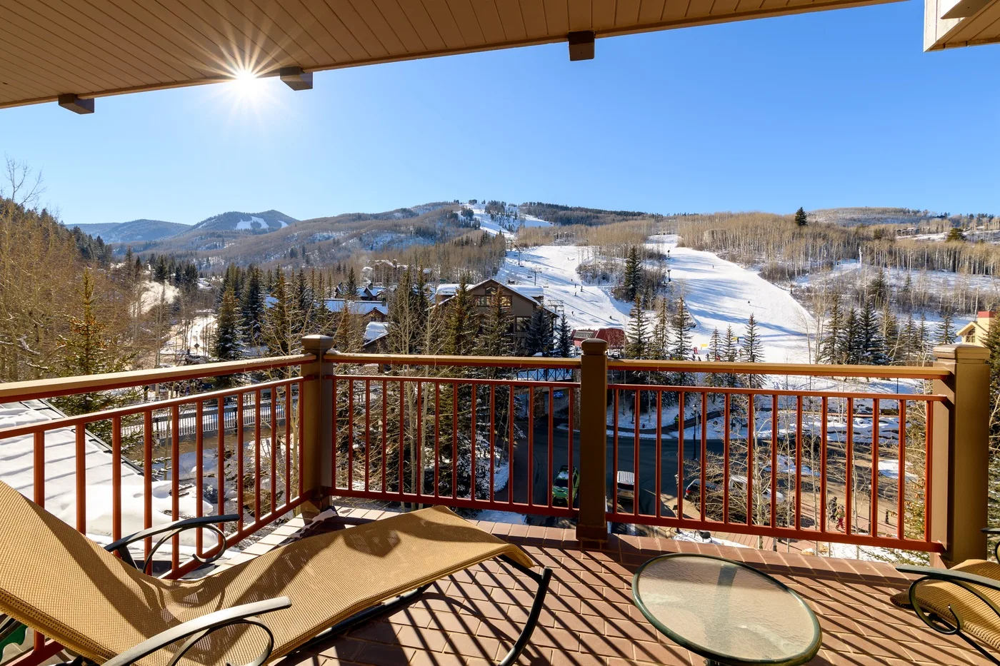 A sunny balcony overlooks snow-covered ski slopes and wooded hills.