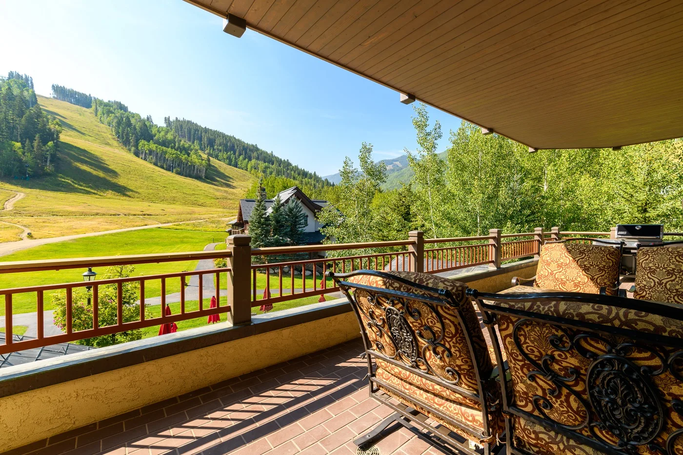 A covered terrace overlooks a green hillside and a small building.