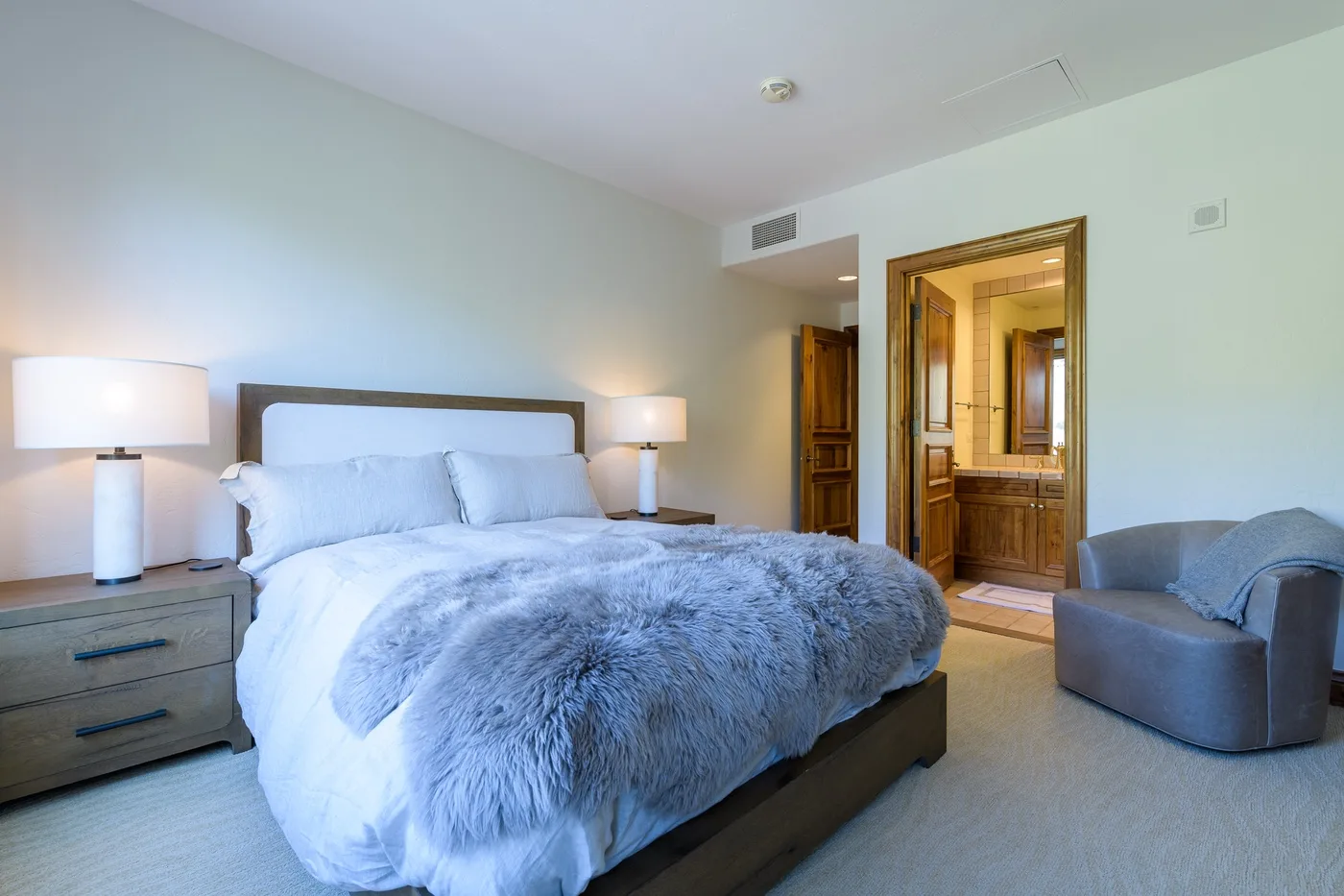 A bedroom with a large bed, bedside lamps, and a doorway to a bathroom.