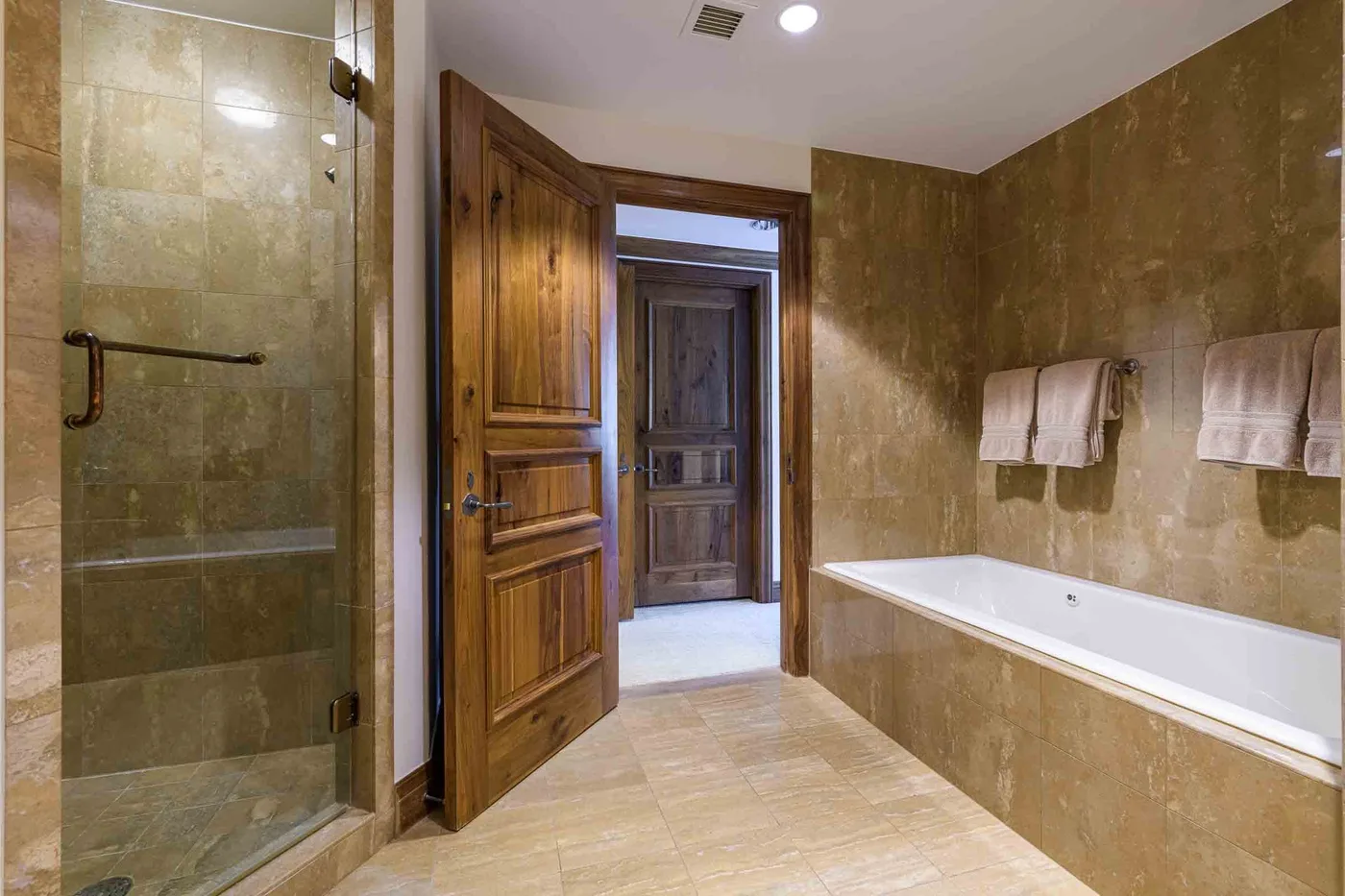 A tiled bathroom with a bathtub, glass shower, and wooden doors.