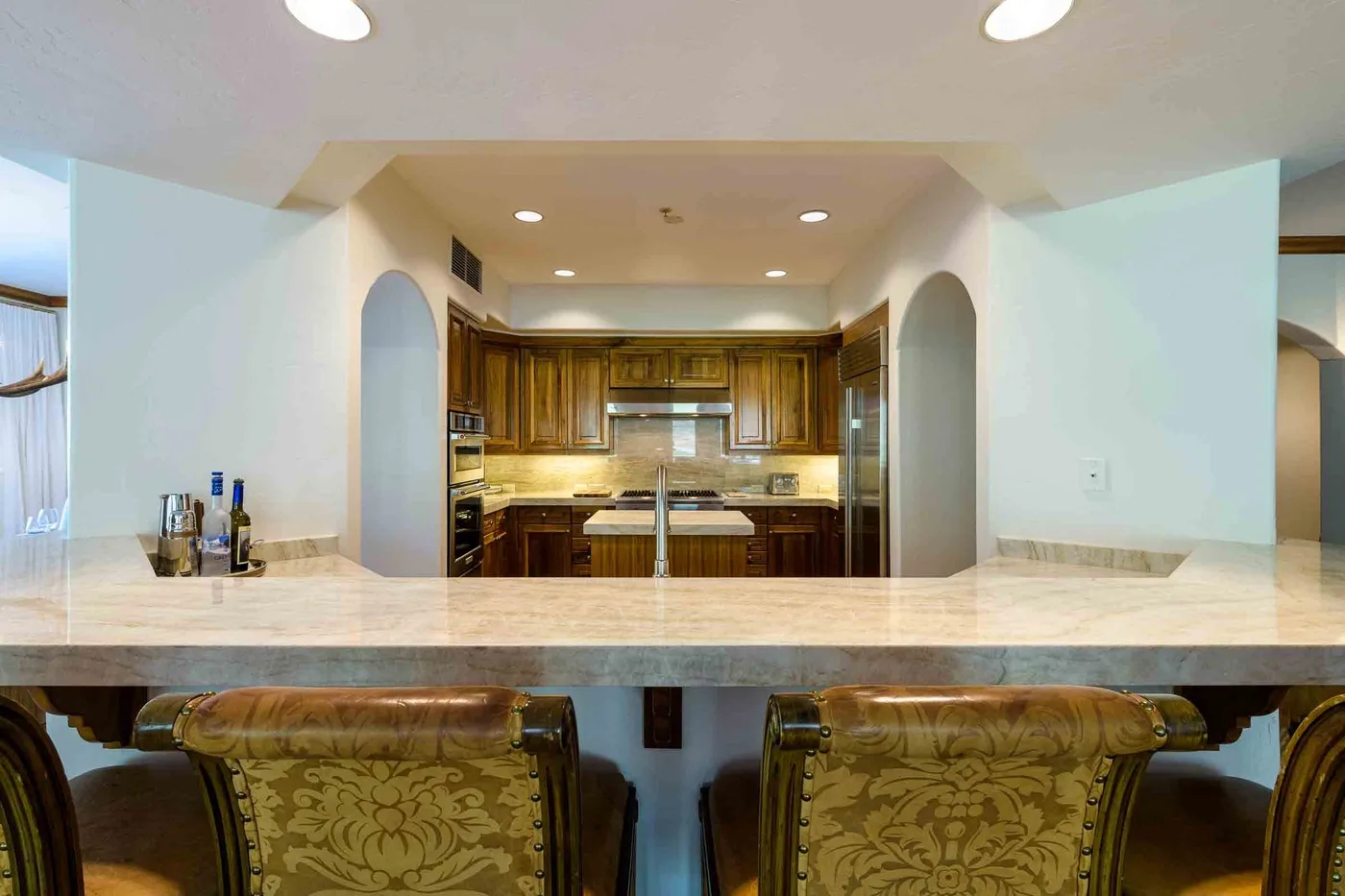 A kitchen with wooden cabinets is visible beyond a wide counter and seating.