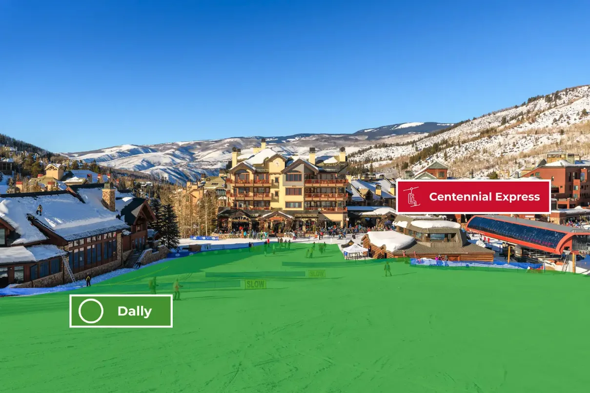 A ski resort village sits below snow-covered mountains beneath a clear blue sky.