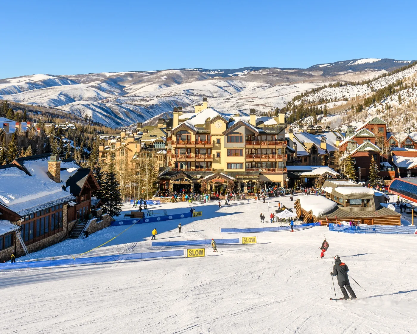 A snowy ski slope runs past resort buildings, with mountain ridges in the background.