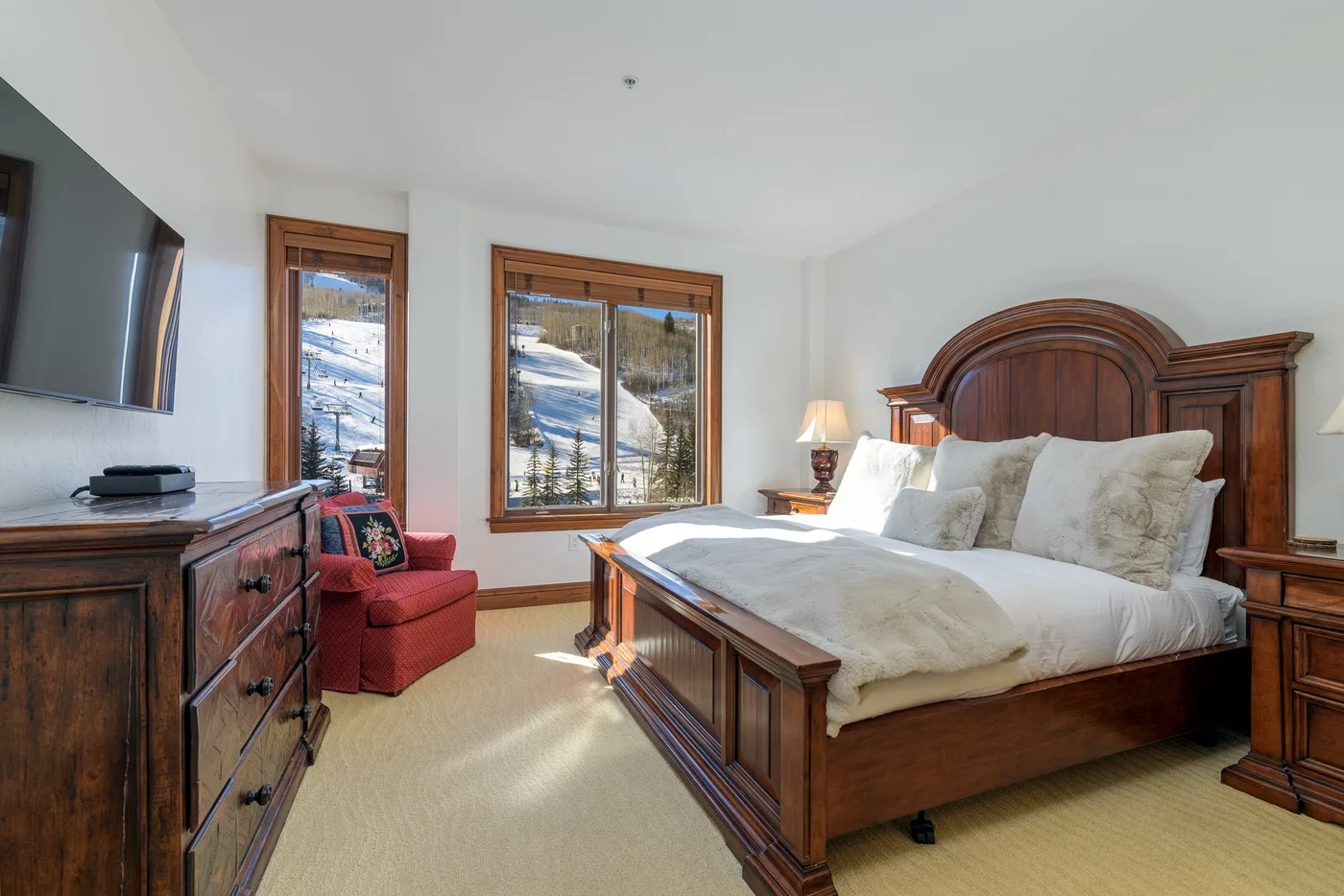 A bedroom with a wooden bed, bedside tables, and windows overlooking a snowy landscape.