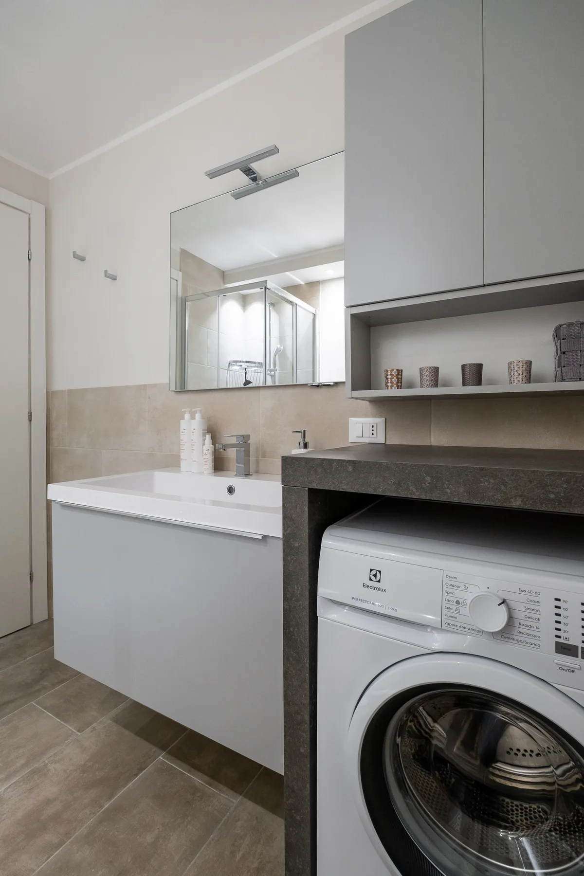 Un baño con lavabo, espejo y lavadora de carga frontal.