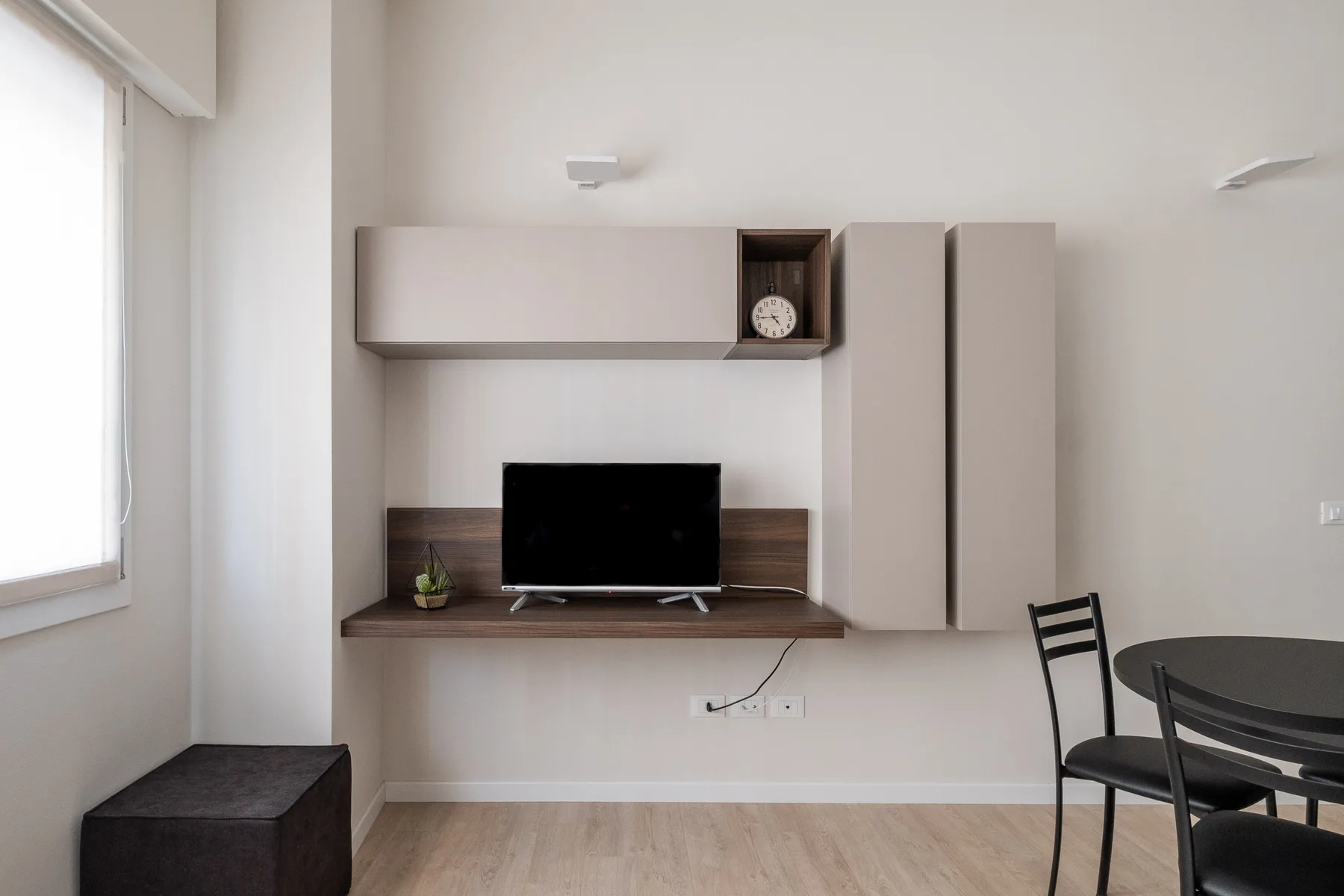 Una sala luminosa con un televisor bajo armarios de pared y una mesa de comedor.