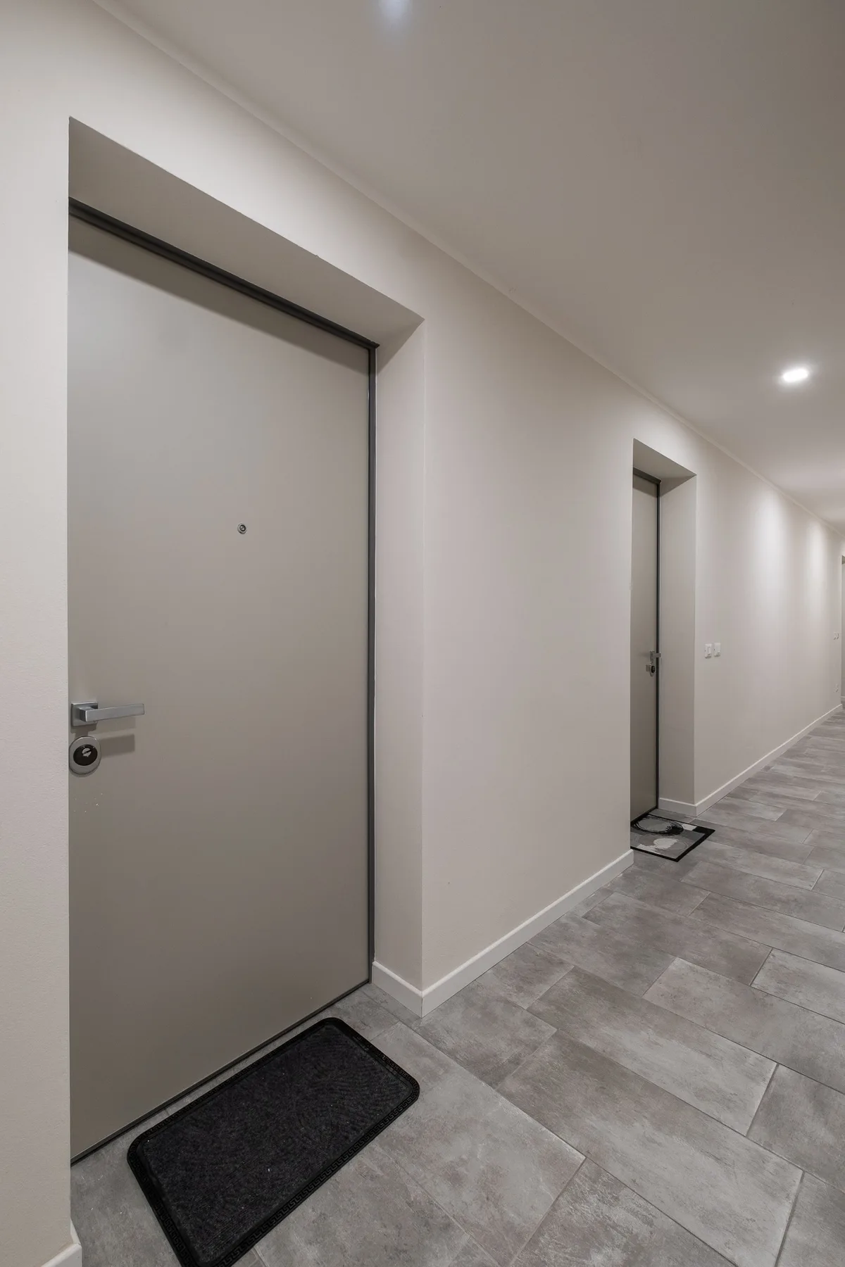 Un pasillo interior con puertas y suelo de baldosas grises.