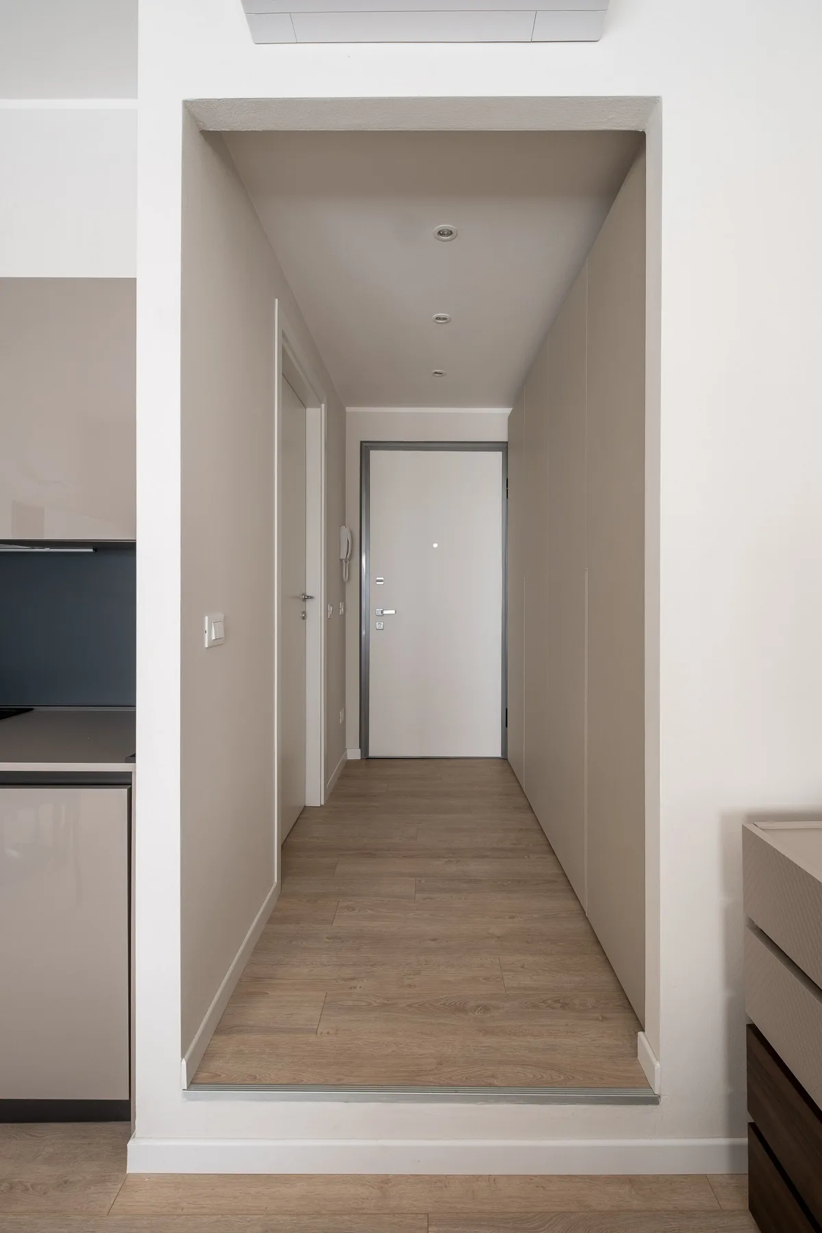 Un pasillo con suelo de aspecto madera conduce a una puerta cerrada.