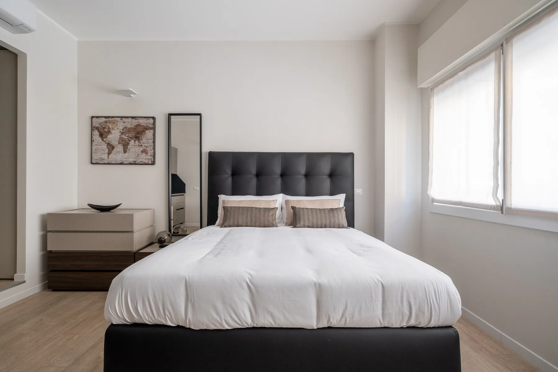 Un dormitorio luminoso con una cama bien hecha y una ventana grande.