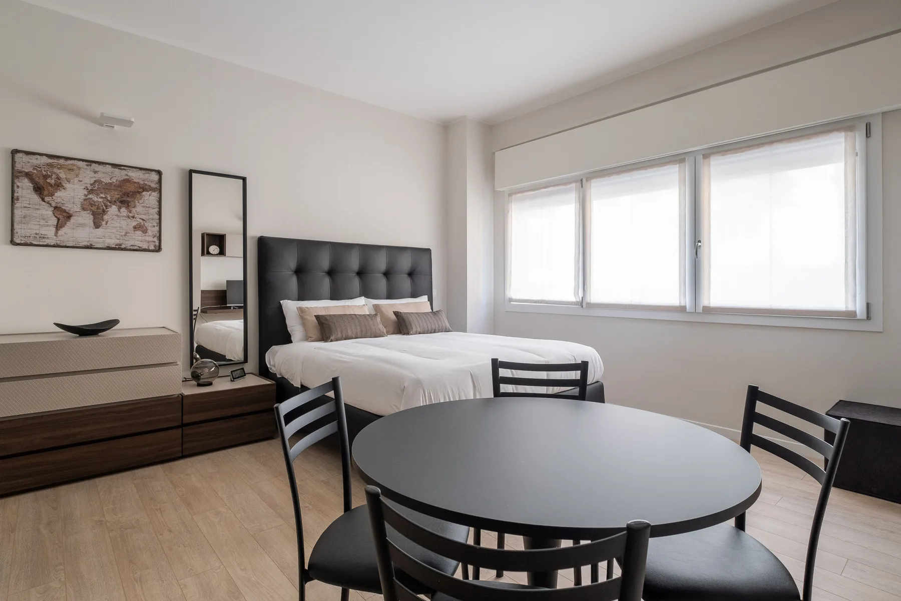 Un dormitorio luminoso con una cama tendida y una mesa redonda.