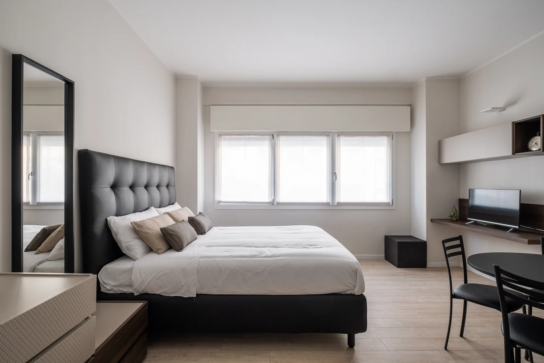Un dormitorio luminoso con una cama junto a un escritorio y ventanas amplias.