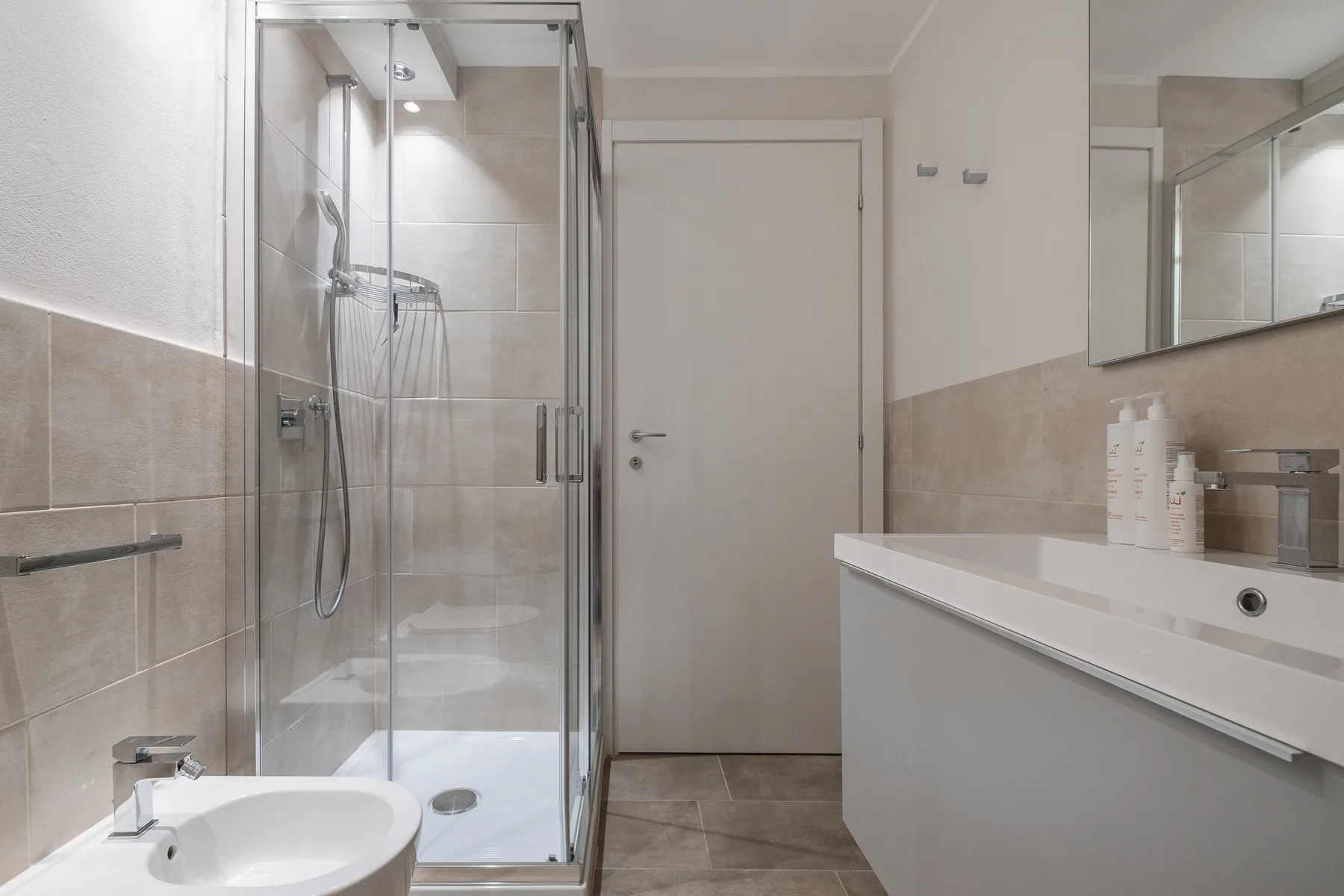 Un baño alicatado con una ducha de vidrio y una encimera larga con lavabo.