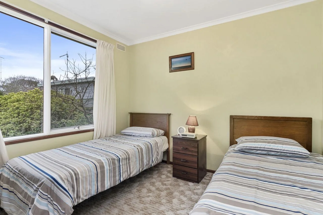 A bedroom with two beds, a bedside table, and a large window.