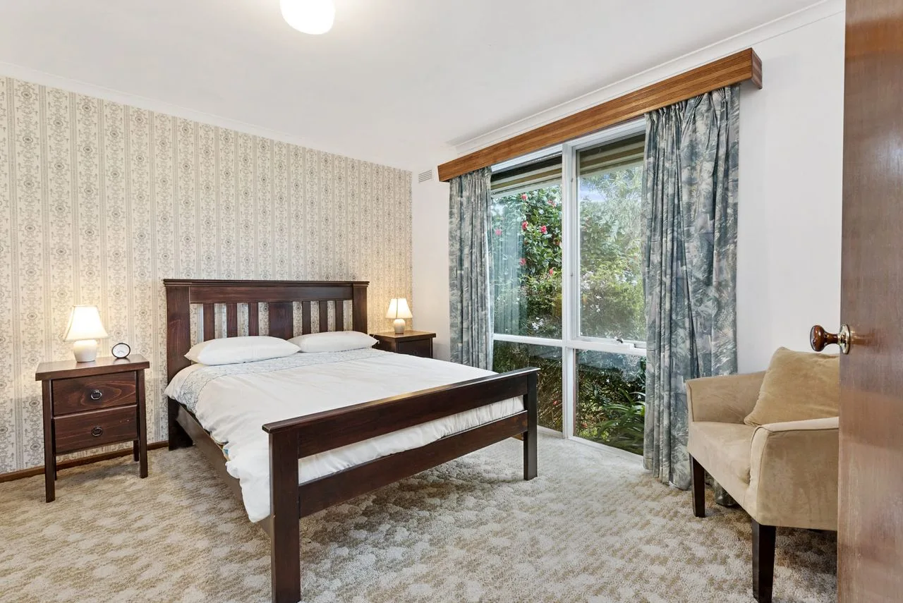 A bedroom with a dark wooden bed, bedside tables, and a large window.