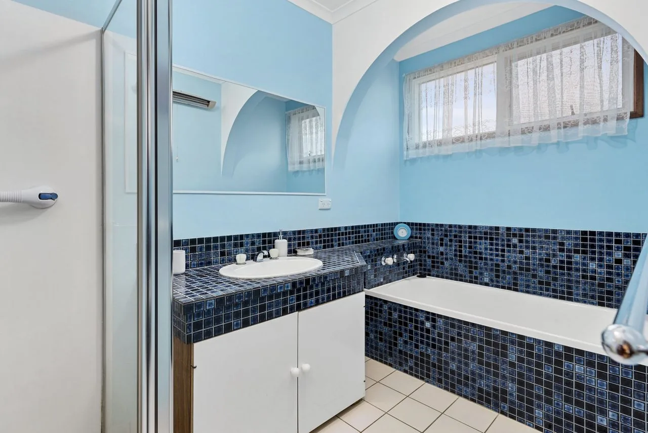A blue-and-white bathroom with a bathtub, sink, and curtained window.