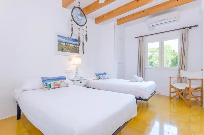 Un dormitorio luminoso con dos camas, vigas de madera y una ventana.