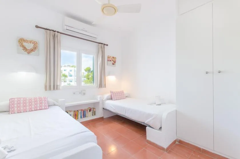 Un dormitorio luminoso con dos camas, una ventana y armarios empotrados blancos.