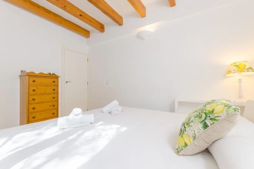 Un dormitorio luminoso con una cama blanca y almohadas estampadas con hojas.