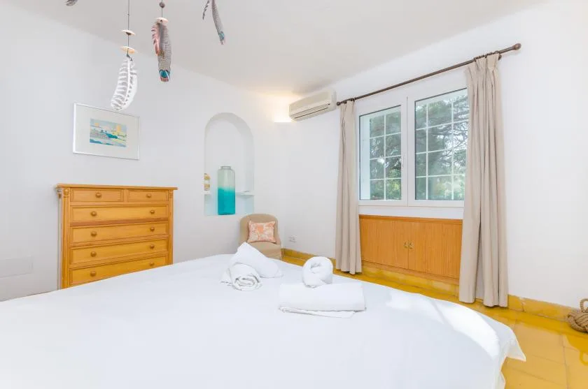 Un dormitorio luminoso con una cama grande, una cómoda de madera y ventanas con cortinas.