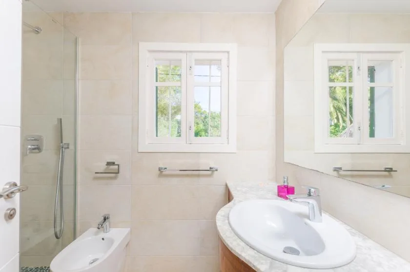Un baño luminoso con azulejos, lavabo, bidé, ducha y ventana.
