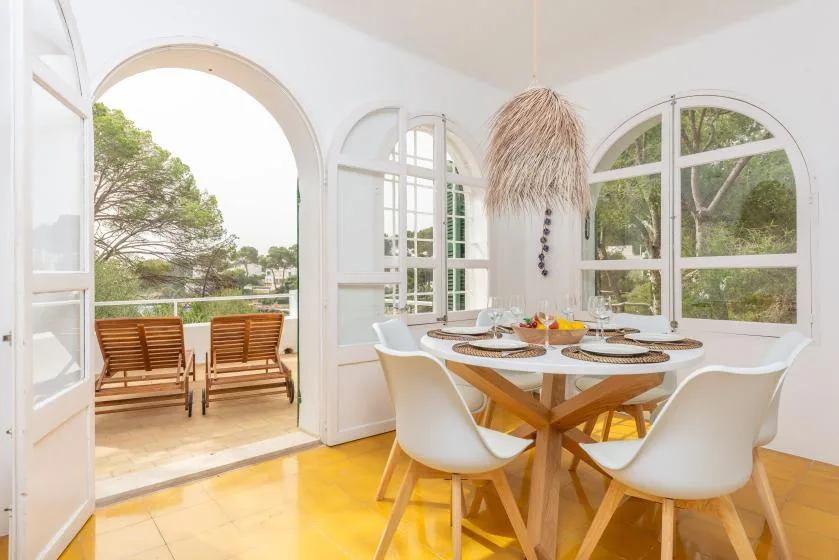 Un comedor luminoso con una mesa de madera junto a grandes ventanas arqueadas.