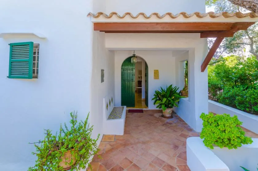 Una entrada cubierta con una puerta verde arqueada y plantas en macetas.