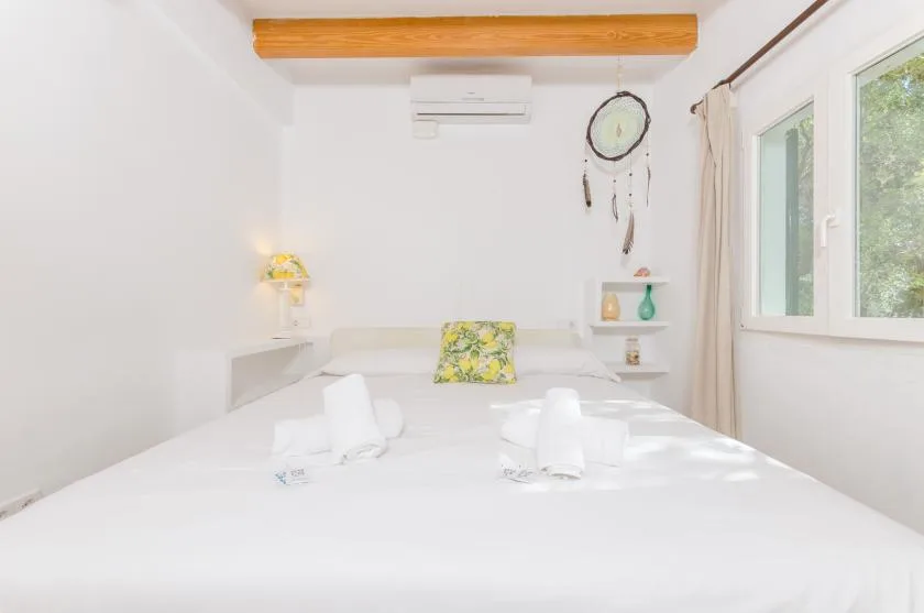 Un dormitorio luminoso con ropa de cama blanca, una ventana y una pequeña repisa.