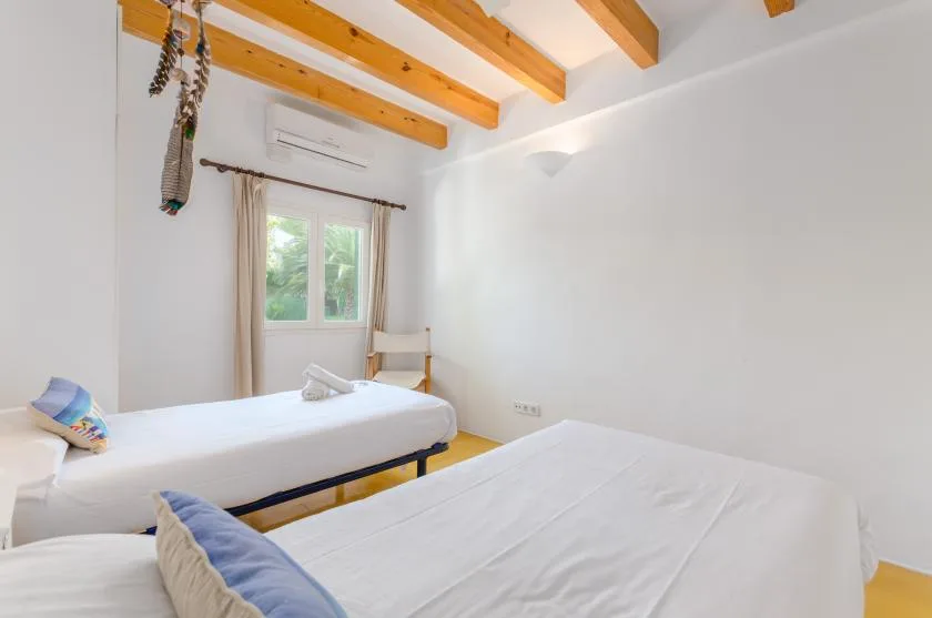 Un dormitorio luminoso con camas bajo vigas de madera vistas en el techo.