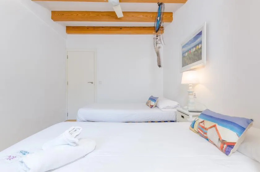 Un dormitorio luminoso con ropa de cama blanca y vigas de madera a la vista.