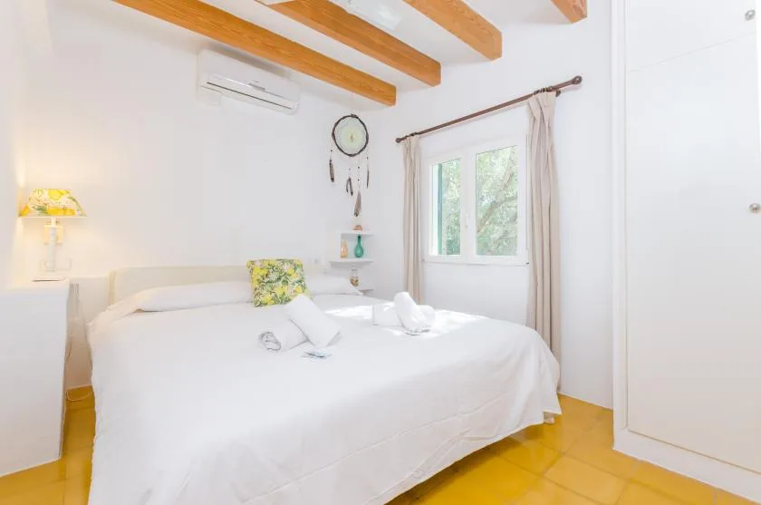 Un dormitorio luminoso con una cama bien tendida junto a una ventana.