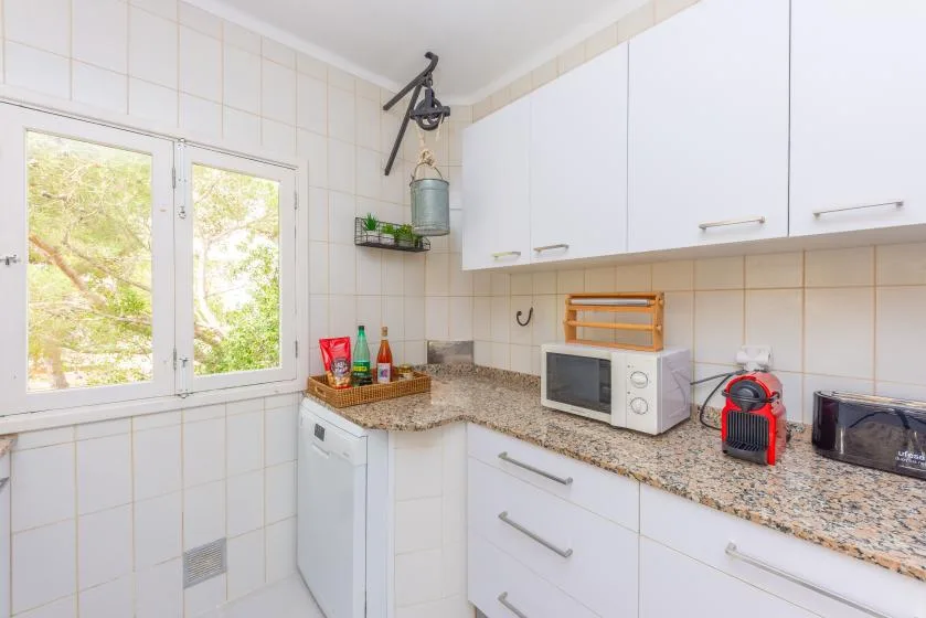Una cocina con azulejos, armarios blancos, una encimera y una ventana.