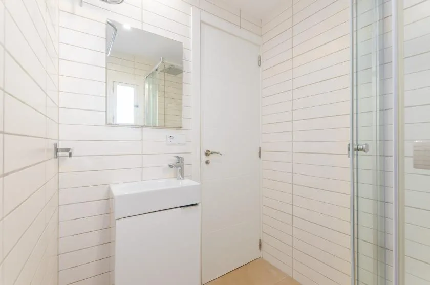 Un baño luminoso con azulejos, lavabo, espejo y ducha de vidrio.