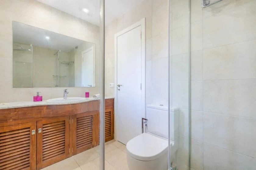 Un baño luminoso con un mueble de madera, espejo y ducha de vidrio.