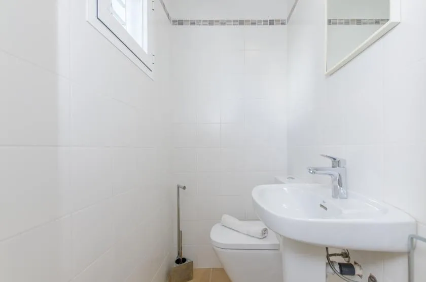 Un baño luminoso con lavabo, inodoro y paredes de azulejos blancos.