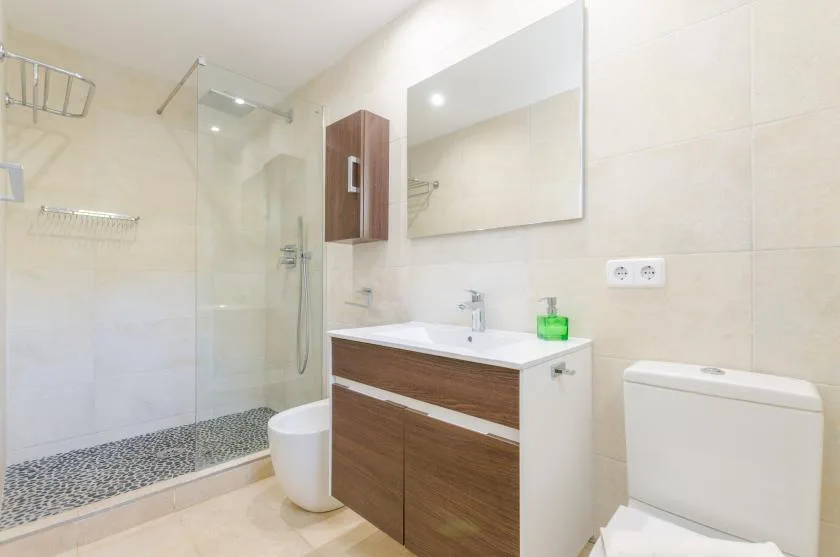 Un baño luminoso con lavabo, espejo, ducha e inodoro.