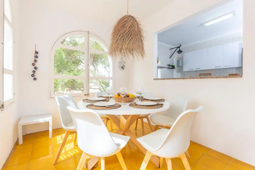 Un comedor luminoso con una mesa redonda y asientos blancos junto a una ventana arqueada.