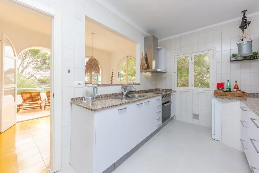 Una cocina luminosa con gabinetes blancos, una encimera y una ventana con vista a la vegetación.