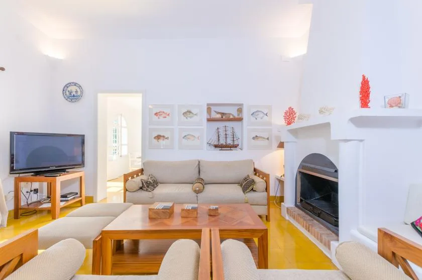 Una sala luminosa con asientos, una mesa de centro de madera, un televisor y una chimenea.