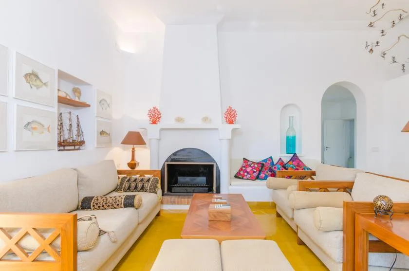 Una sala de estar luminosa con asientos dispuestos alrededor de una chimenea y una mesa de centro.
