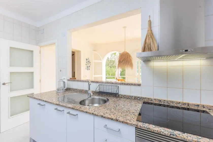 Una cocina luminosa con encimera de aspecto pétreo y un fregadero bajo una amplia abertura.