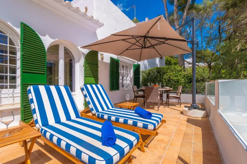 A sunny patio has striped loungers beneath a large umbrella.