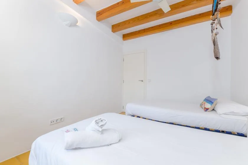 Un dormitorio luminoso con ropa de cama blanca y vigas de madera expuestas en el techo.