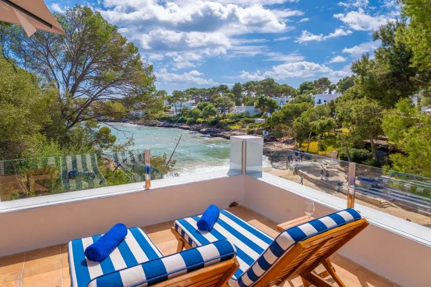 A seaside terrace with striped loungers overlooks a tree-lined bay.