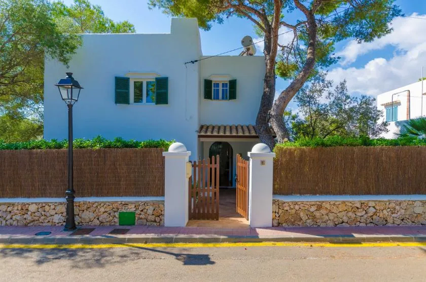 Una casa blanca está detrás de una puerta de madera abierta, con árboles encima.