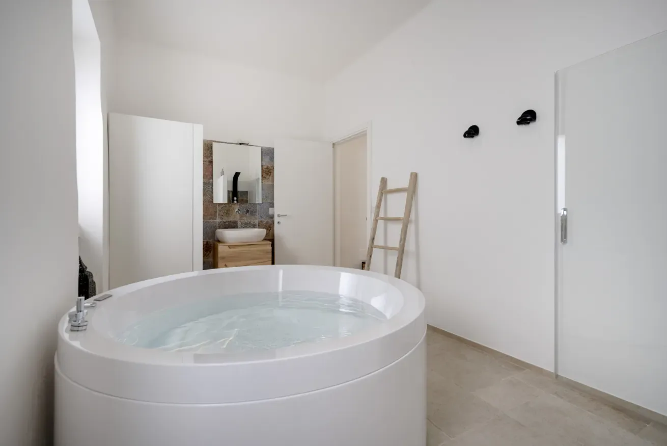 A bright bathroom with a large round soaking tub and a sink in the background.