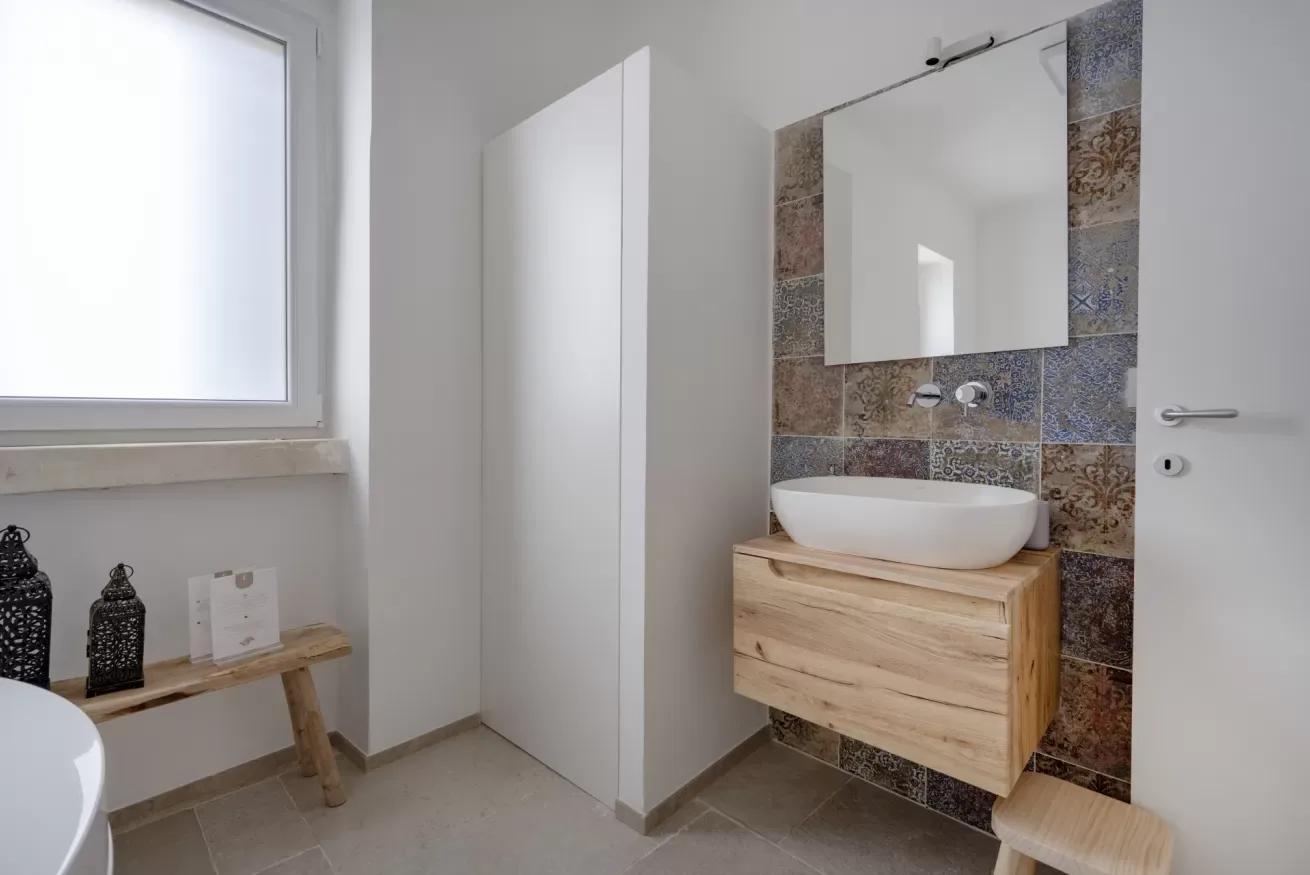 A bathroom with a vessel sink, wood vanity, and tiled wall.