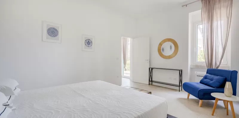 A bright bedroom with a bed, blue seating, and a small console table.