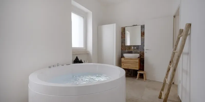 A bright bathroom with a large round tub and a vanity.