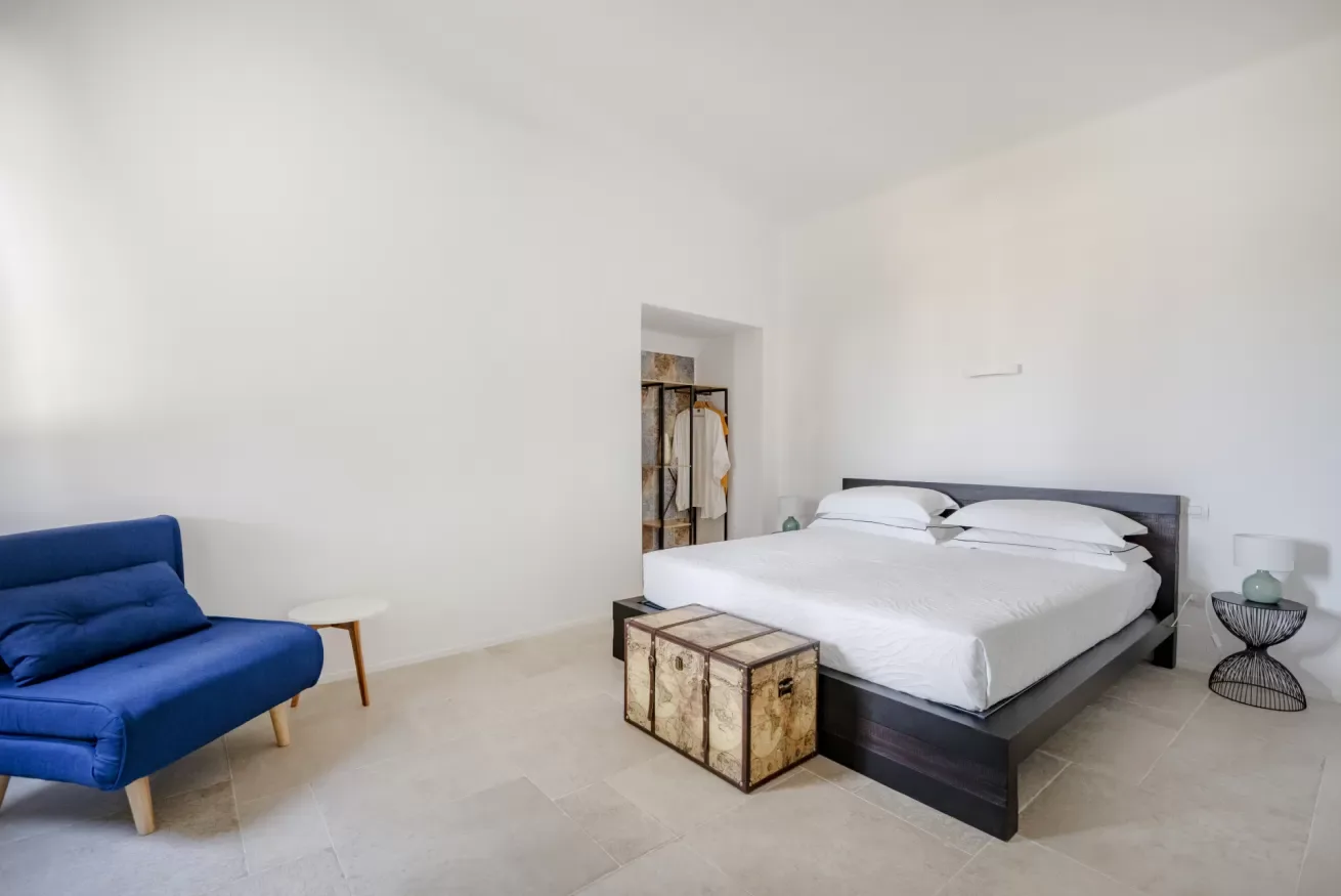 A bright bedroom with a bed and a blue sofa.