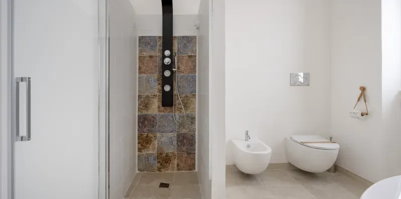 A bathroom with a shower, toilet, and wall-mounted sink.